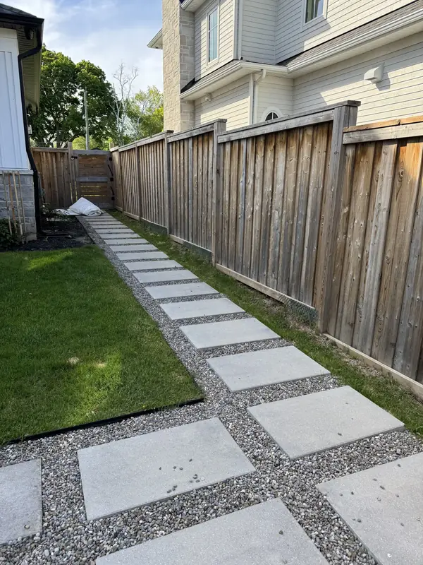 Side yard walkway of large concrete slabs set in gravel beside a cedar fence
